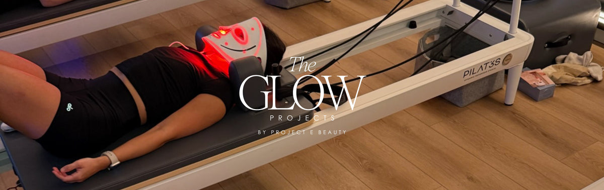 Person lying on a Pilates reformer at The Glow Projects by Project E Beauty, wearing an LED red light therapy mask for skincare during fitness recovery.